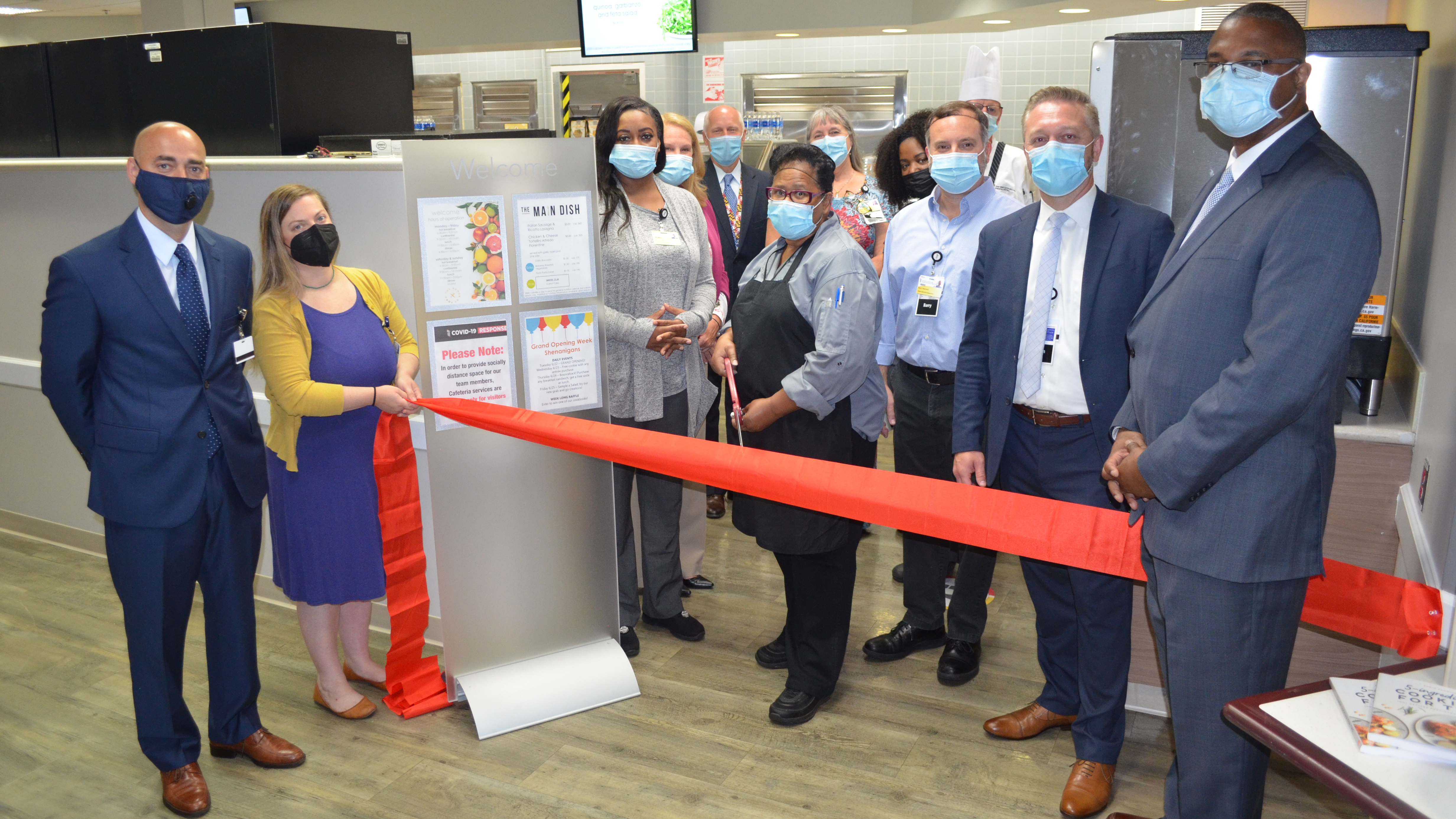 A group stands in front of the Easton hospital cafeteria and one woman readies to cut the red ribbon for the grand-opening of the new Easton Marketplace, following renovations to the cafeteria