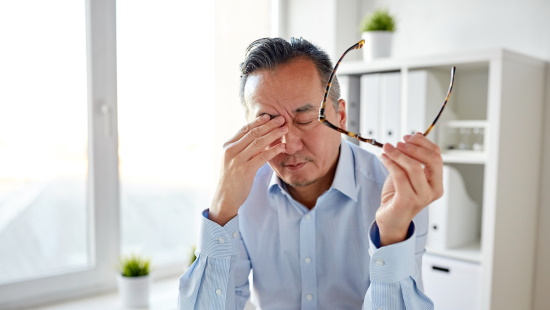 Man rubbing his eyes and holding glasses