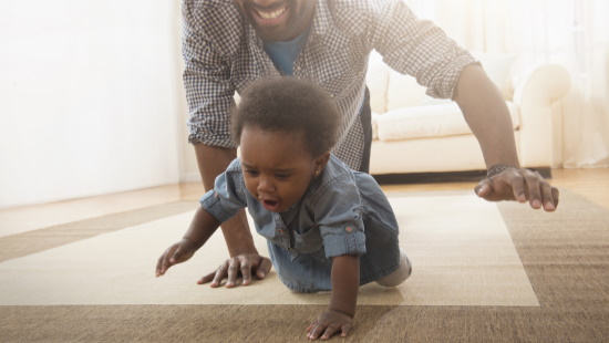 Baby crawling with father behind
