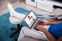 patient with foot cast on laptop for dr. appointment