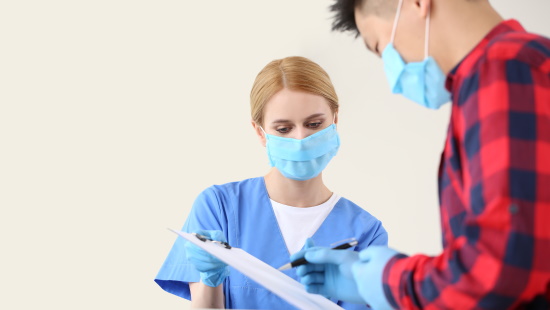 Healthcare worker and visitor, wearing masks, filling out forms