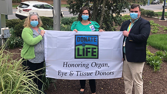 Three people stand holding the Living Legacy Foundation flag.