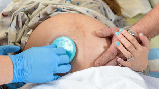 Woman holding man's hand while medical staff listen to her pregnant belly with stethoscope