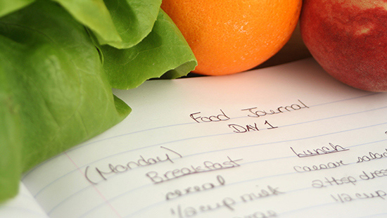 Assorted fruits and vegetables around a piece of page that says 'food journal: day 1'